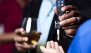 Homem com drink em mãos entregando chaves do carro para outra pessoa